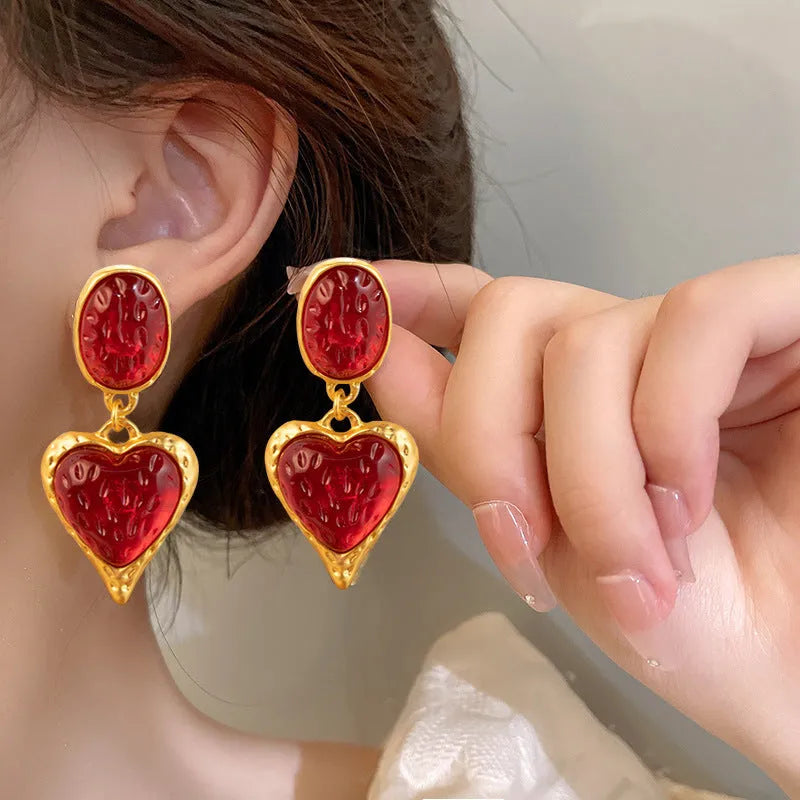 Close-up of oval love heart stud earrings with pleated needle posts in green, purple, red, and yellow-white colours.