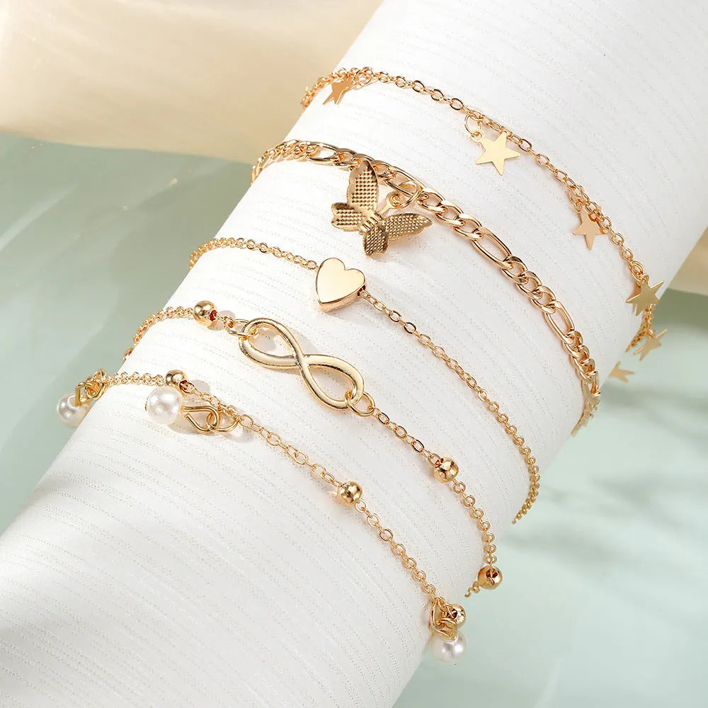 Set of four alloy anklets with butterfly, pearl, and heart designs on a white background.