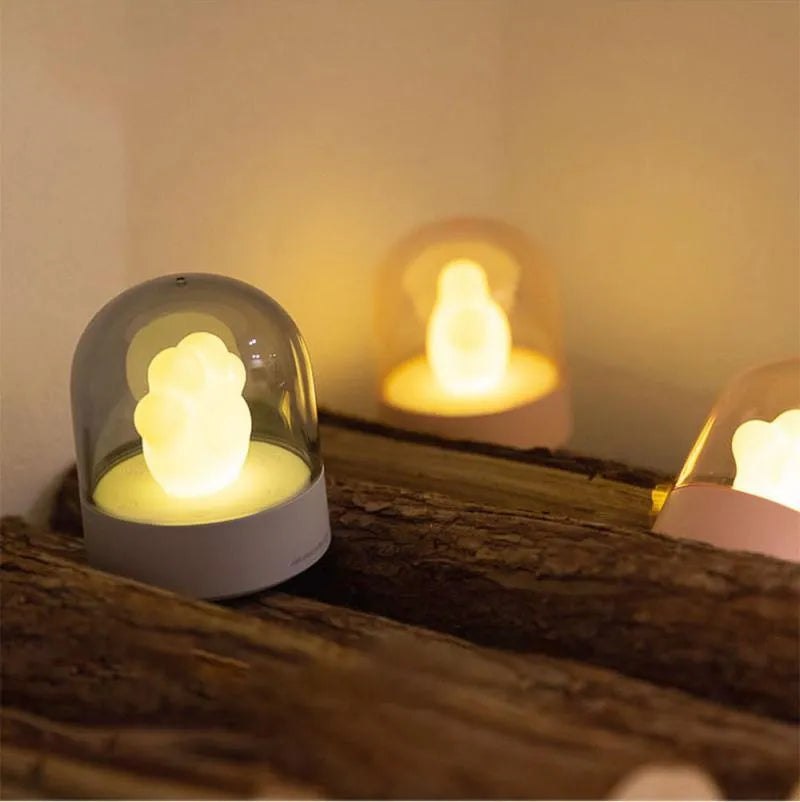 Grey and pink cat paw shaped USB night light with rotating lighting and music box features on desktop