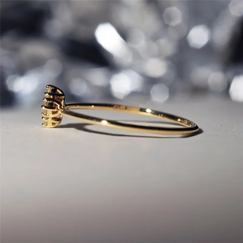 Four heart-shaped motif gold rings with zircon stones set on a dark surface