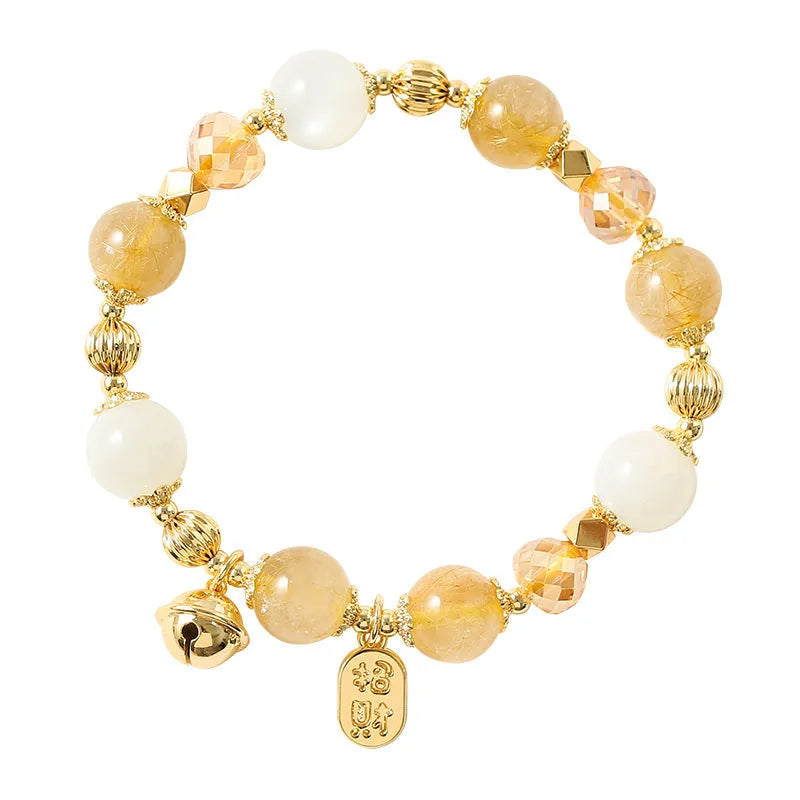 Gold-coloured rutilated quartz bracelet with a ringing bell charm on a wrist.