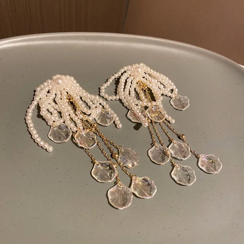 Gold long drop earrings with pearl, bow, tassel, and sequin detail on white background