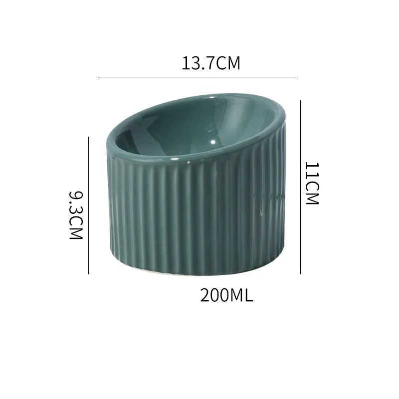Ceramic elevated cat bowl in light green, showing its tilted, round shape and raised design on a table.