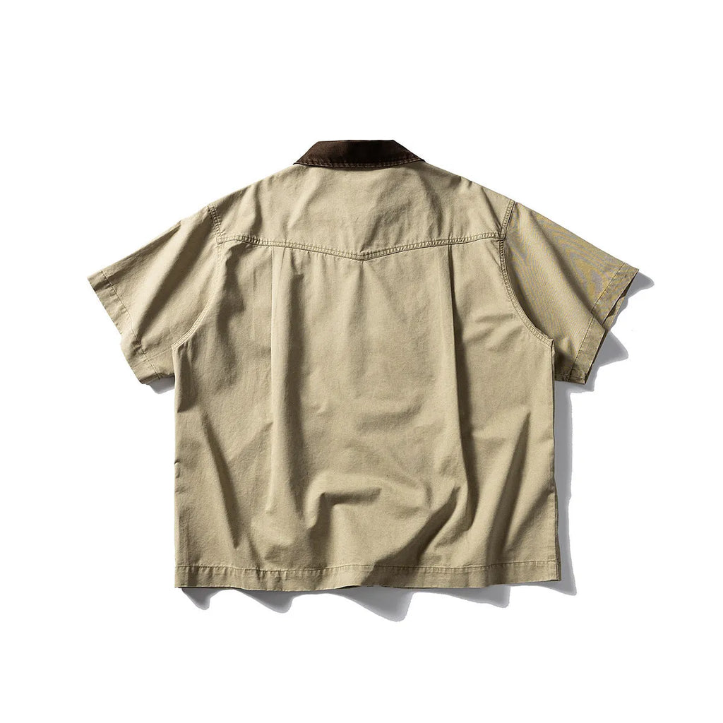 A man's khaki loose-fit short-sleeve cotton overalls shirt with button front and patch pockets.