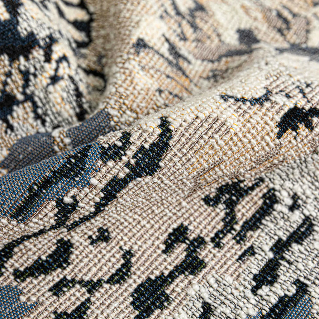 Antique blue square cushion with abstract botanical flower pattern on a grey sofa.