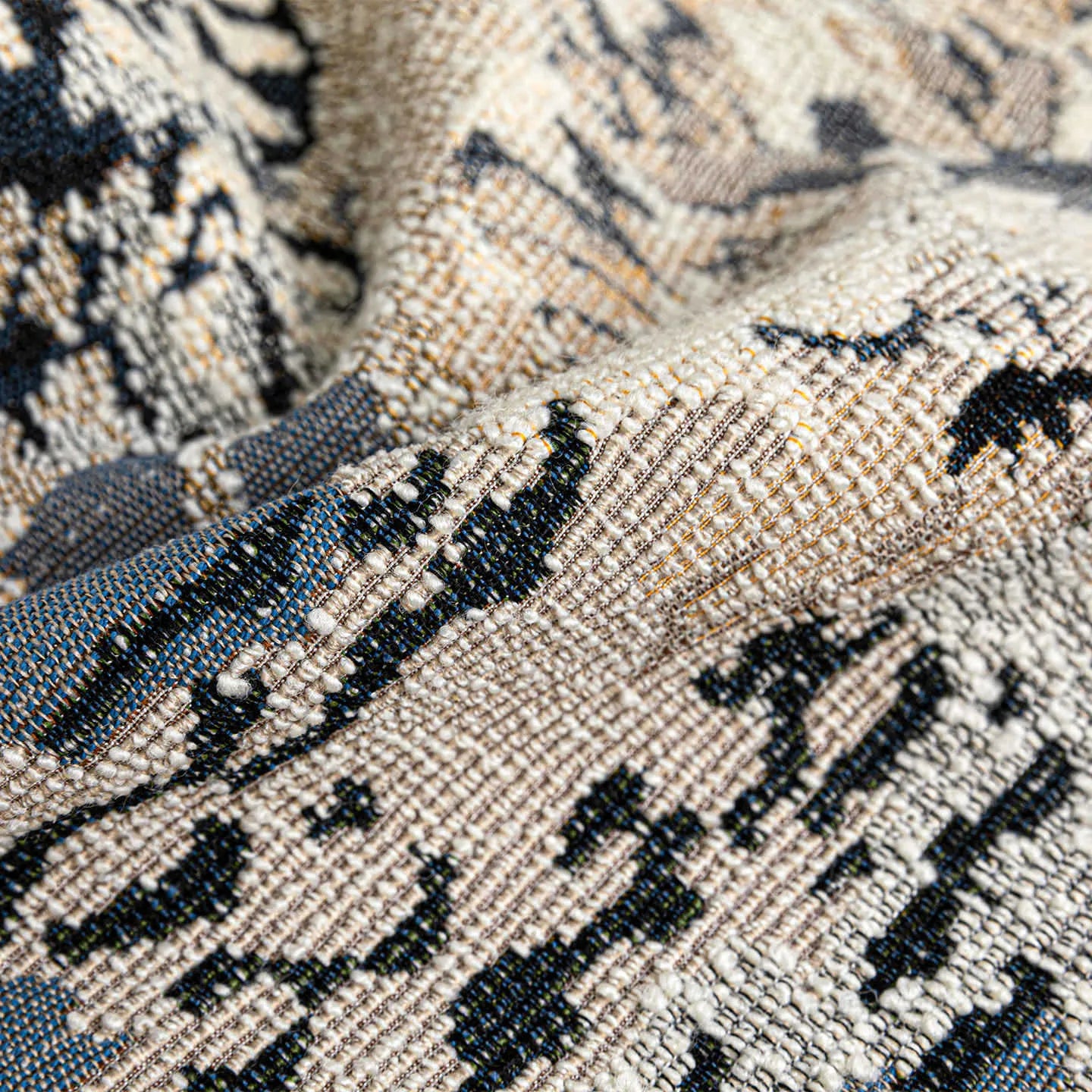 Antique blue square cushion with abstract botanical flower pattern on a grey sofa.