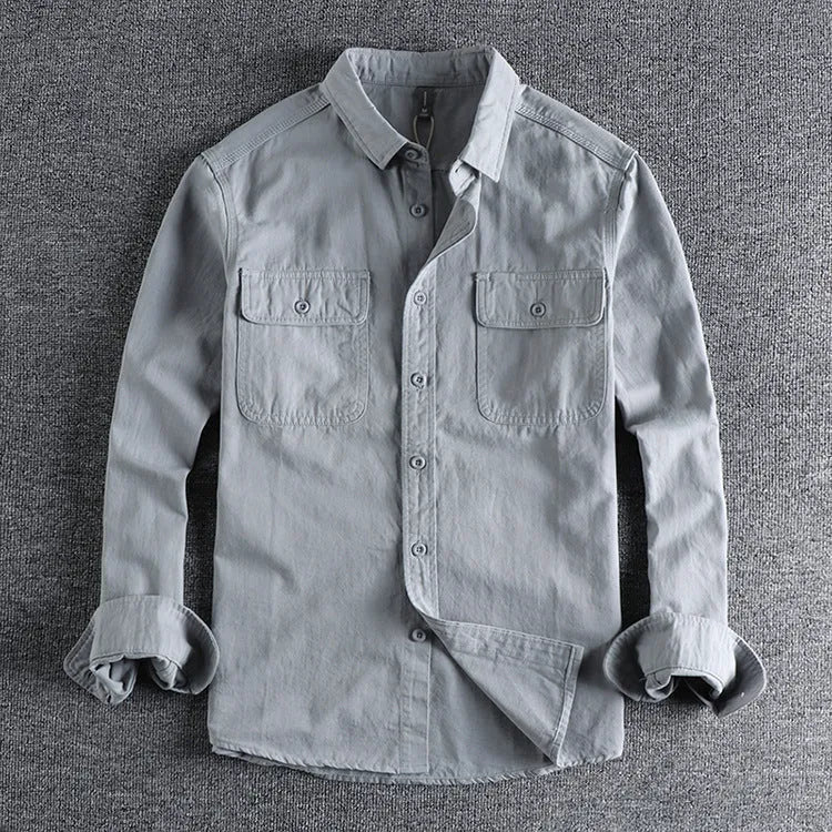 Man wearing a loose grey long sleeve shirt with a cardigan and overalls-inspired design