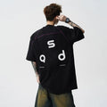 Men's loose-fit black cotton t-shirt with a white printed letter design on the front, showing short sleeves and a round neck.
