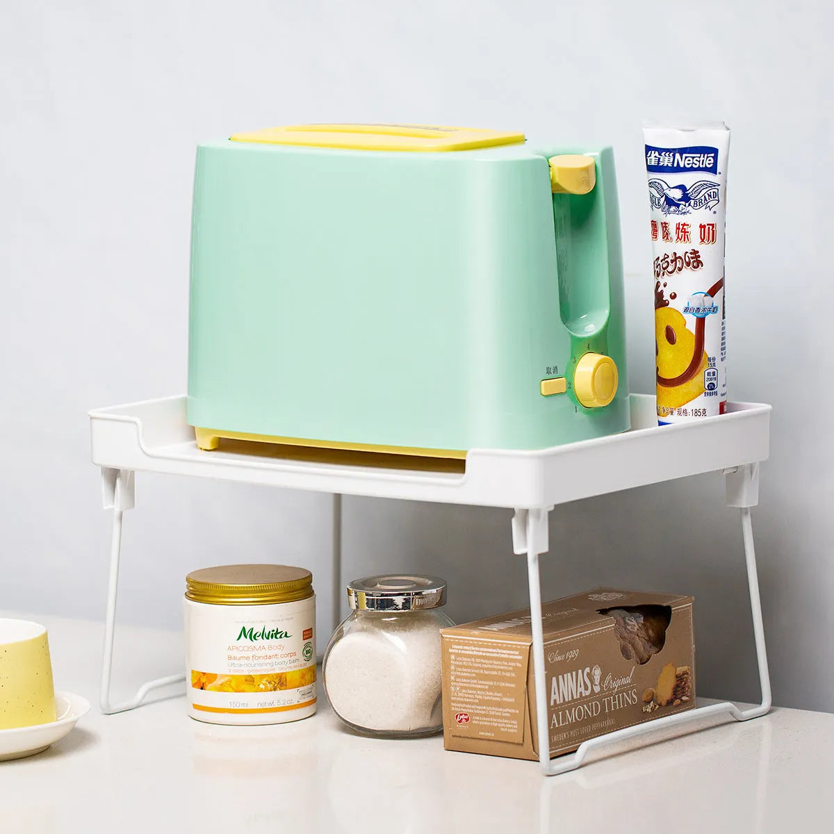 A transparent plastic kitchen storage rack holding utensils and spice jars on a countertop.