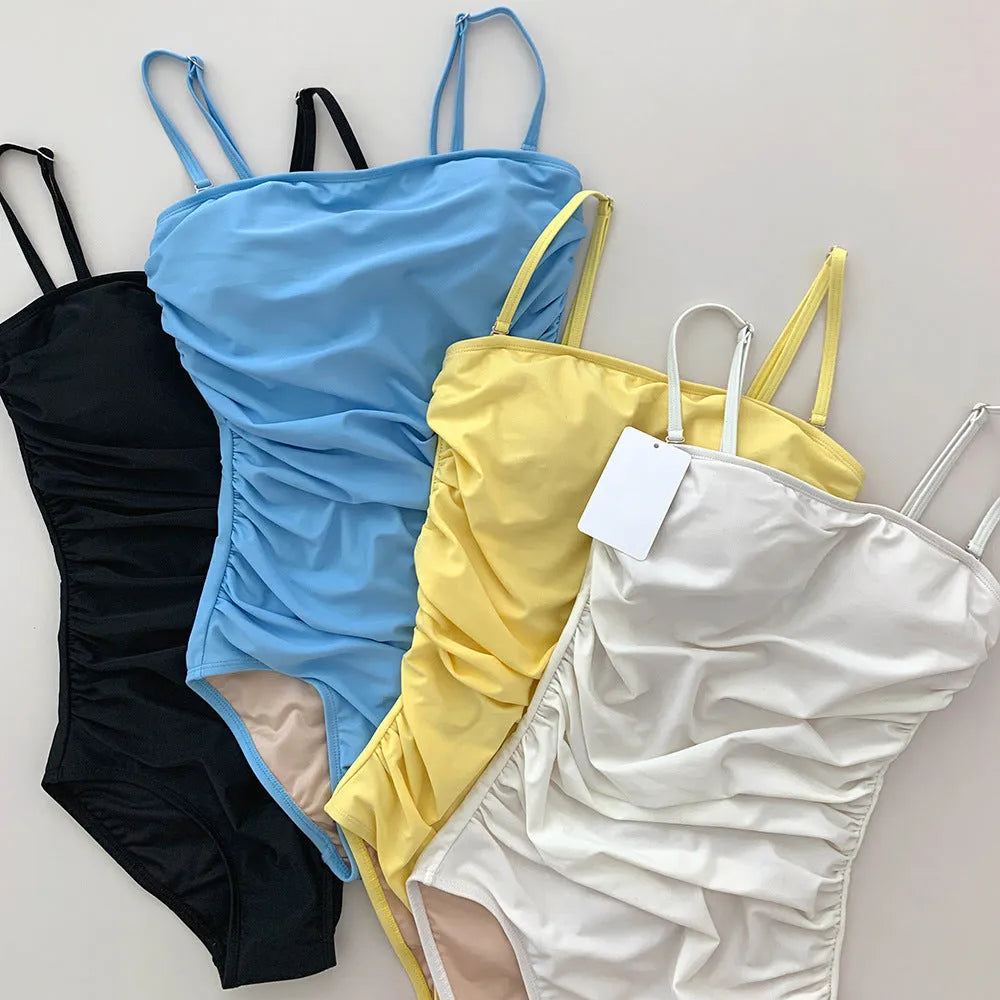 Sling style one-piece swimsuit for women with belly pleats in blue, white, yellow, or black.