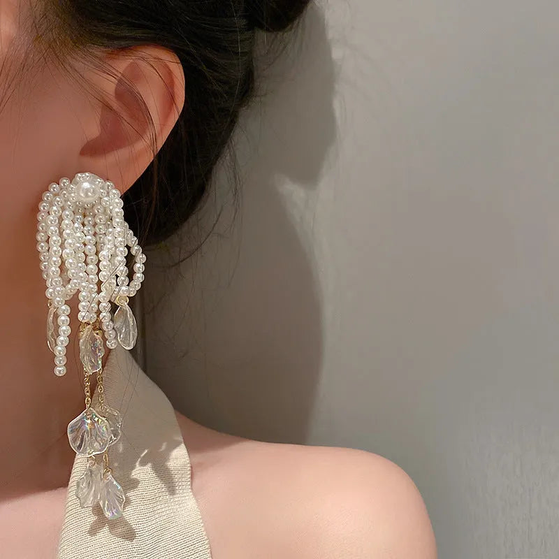 Gold long drop earrings with pearl, bow, tassel, and sequin detail on white background