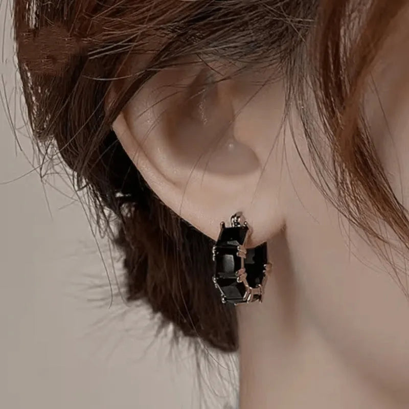 A pair of geometric U-shaped gold ear rings with round details and black zircon crystals.
