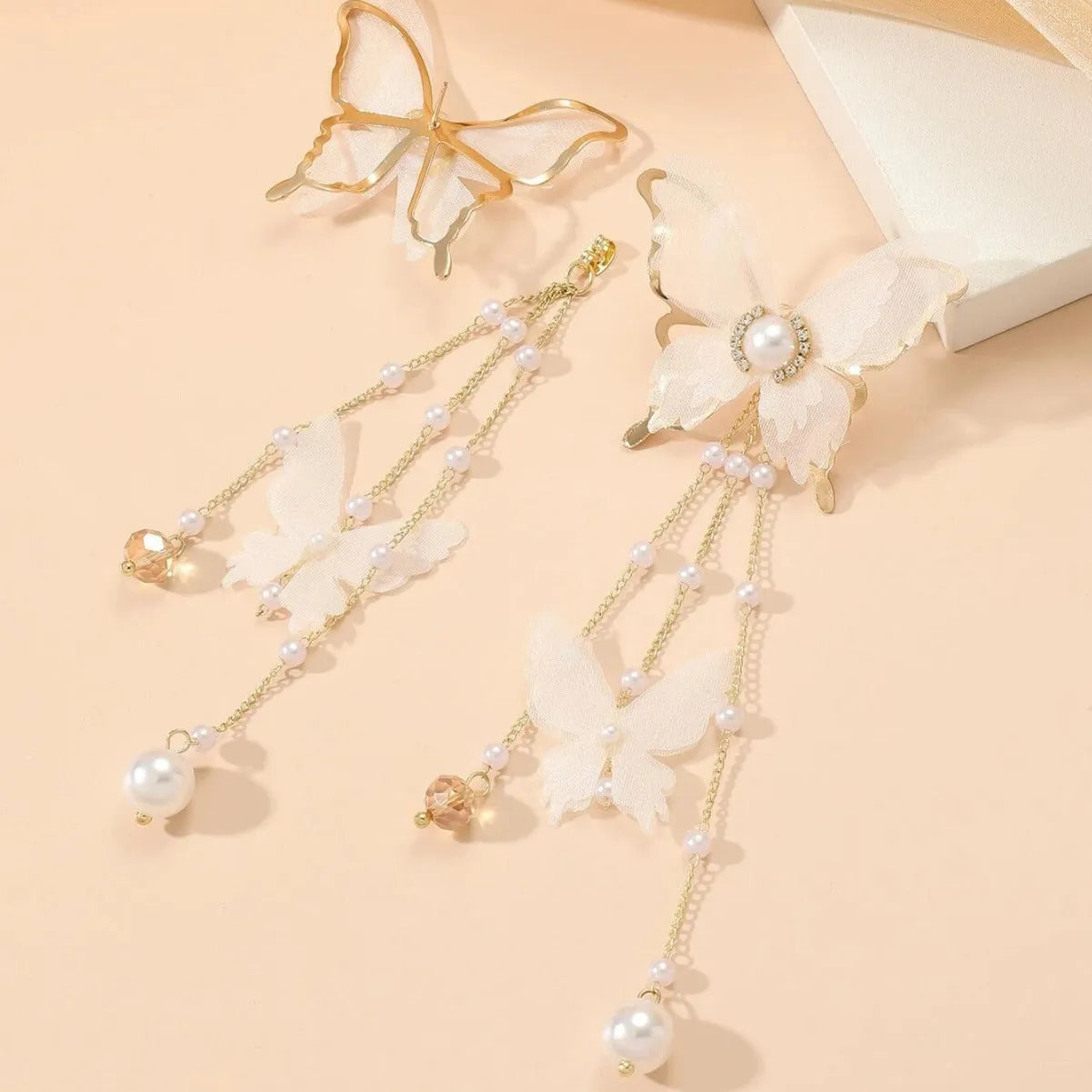White butterfly-shaped drop earrings with pearls, rhinestones, and tassel lace details on a model.