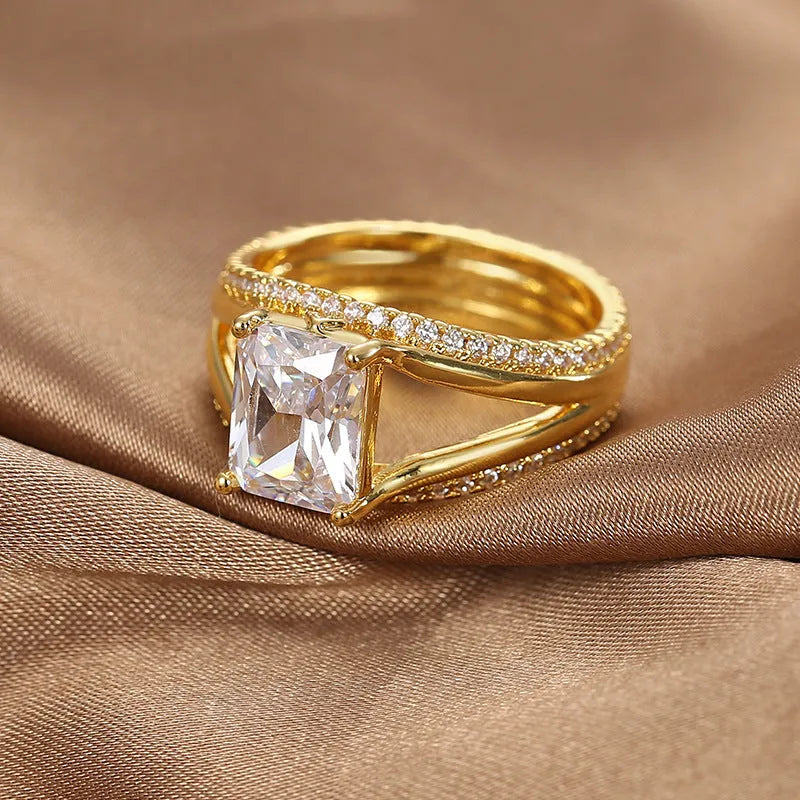 Gold-colour geometric women's ring with a square zircon centre, shown on a finger.