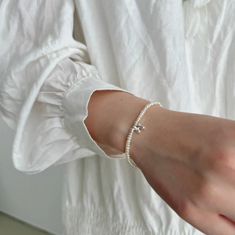 Women's natural freshwater pearl bracelet in 925 silver with letter shape charm on neutral background