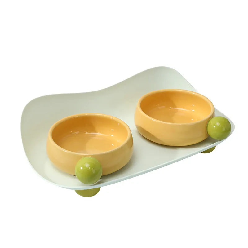 Pink and yellow elevated ceramic pet bowl set for food and water on a non-slip base.