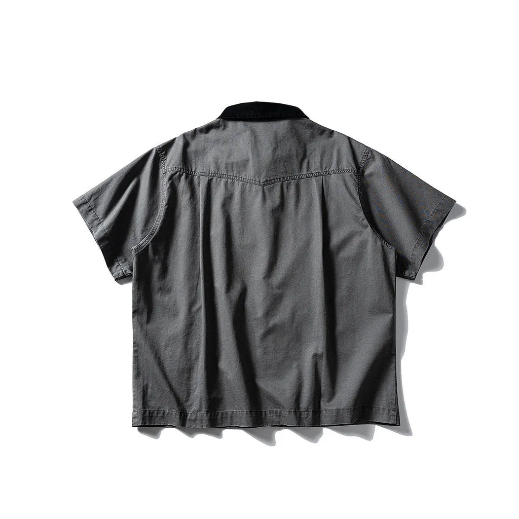 A man's khaki loose-fit short-sleeve cotton overalls shirt with button front and patch pockets.