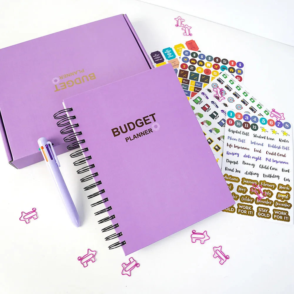 Purple coil-bound financial planning notebook with stickers, pen, and paper clips for monthly budget tracking