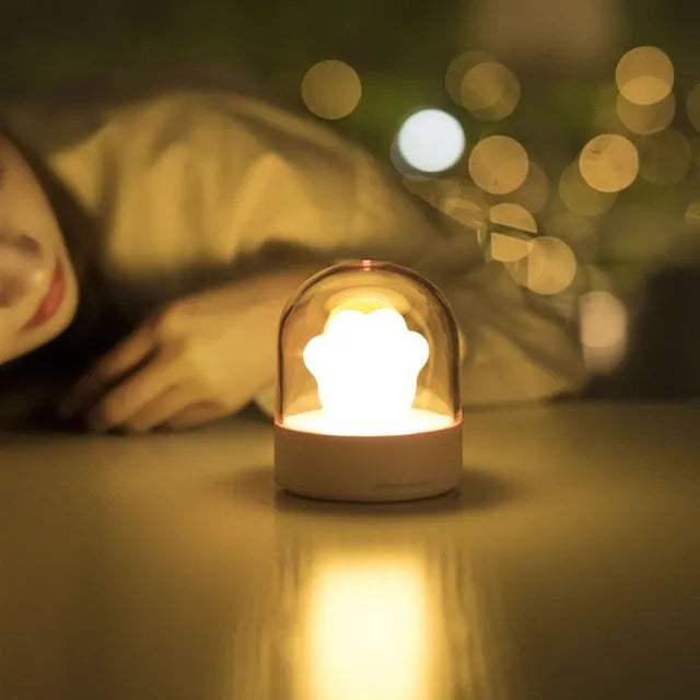Grey and pink cat paw shaped USB night light with rotating lighting and music box features on desktop