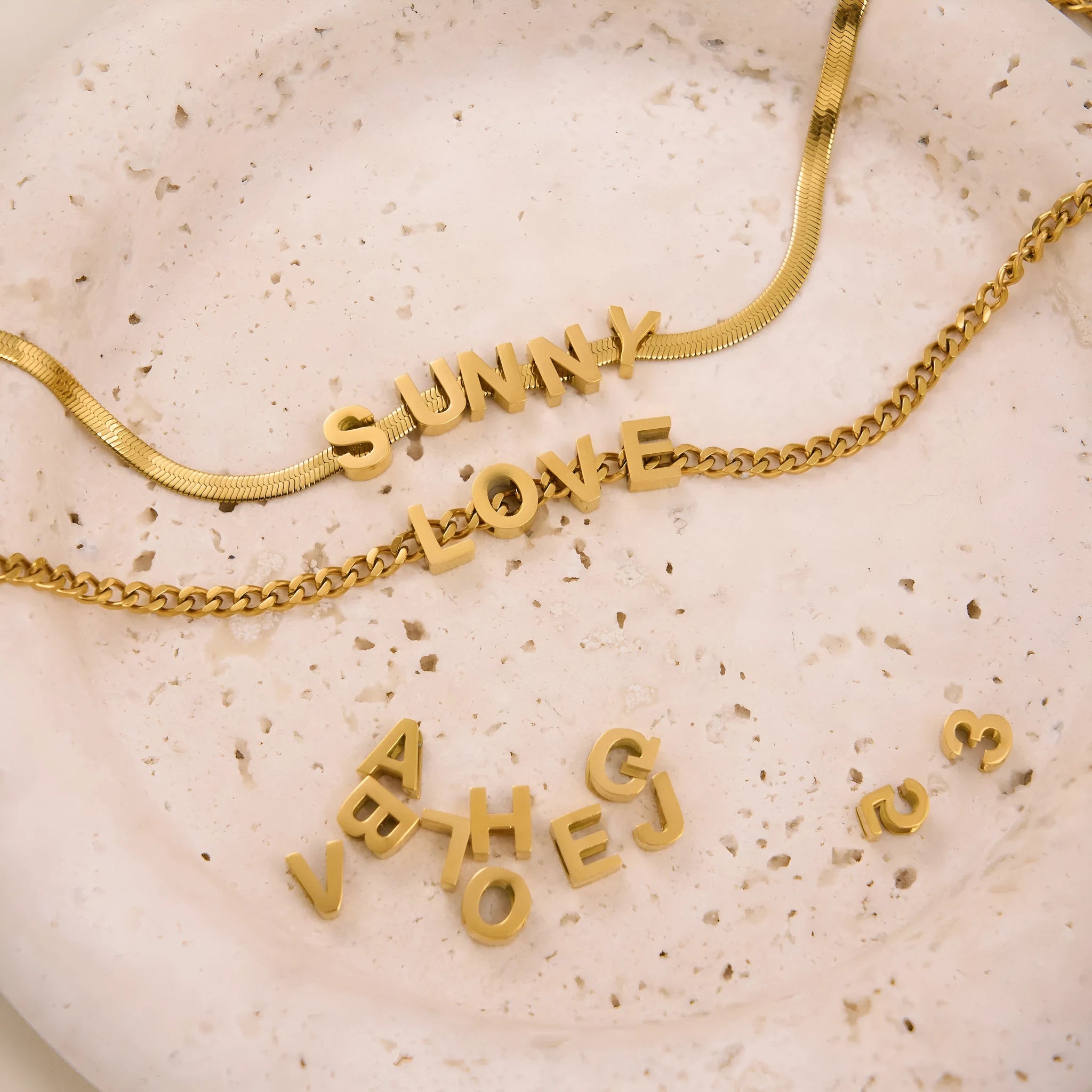 Gold and silver titanium steel necklaces showing letter A, number 7, and love heart charms on a 40.5cm chain.