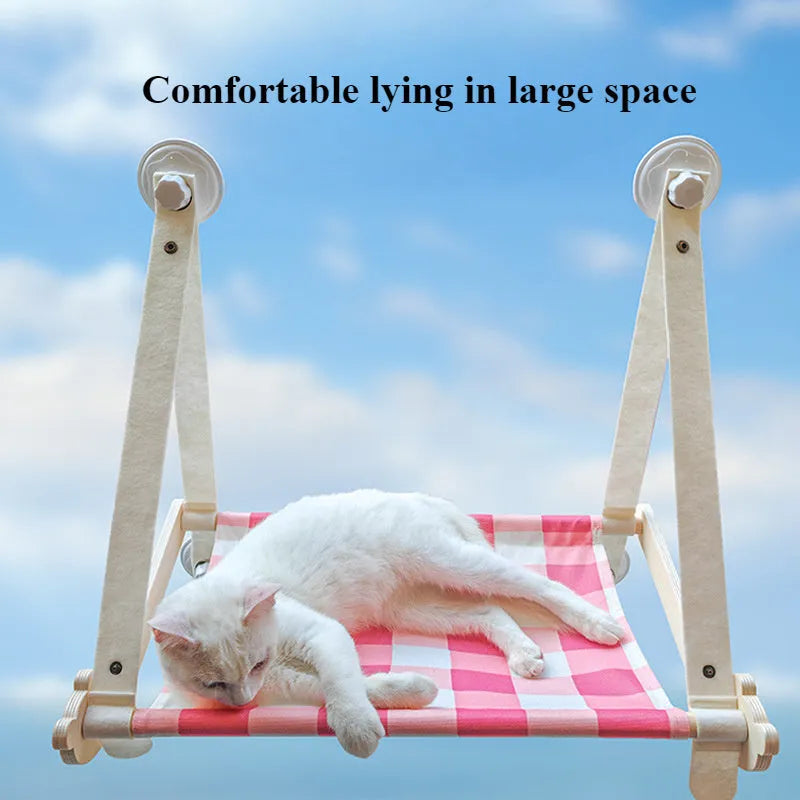 Pink wooden cat hammock with suction cups attached to a window, showing a removable cat paw print fabric seat.