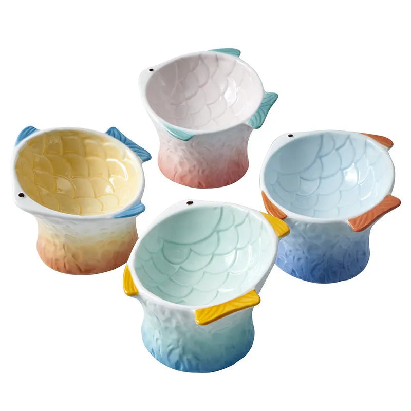 Set of four blue fish-shaped ceramic cat bowls with a tilted angle on a flat surface.