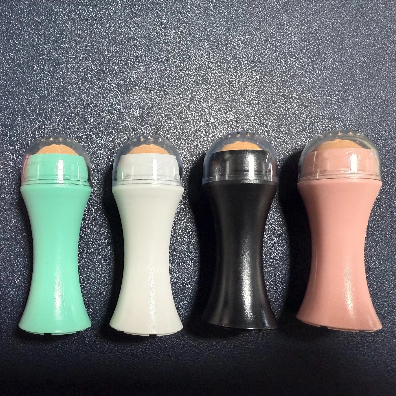 Portable volcanic stone roller for absorbing facial oil, shown in black, green, pink, and white colour options.