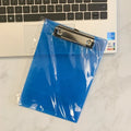 A4 transparent plate clipboard with metal clip, shown in blue colour on a desk with paper.