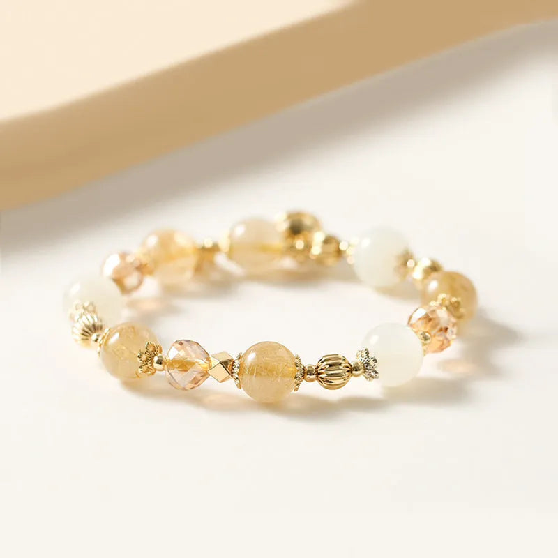 Gold-coloured rutilated quartz bracelet with a ringing bell charm on a wrist.
