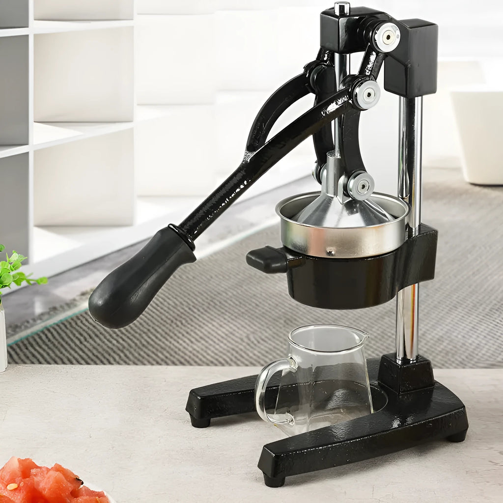 Black cast iron manual juice extractor with stainless steel strainer on a kitchen counter.
