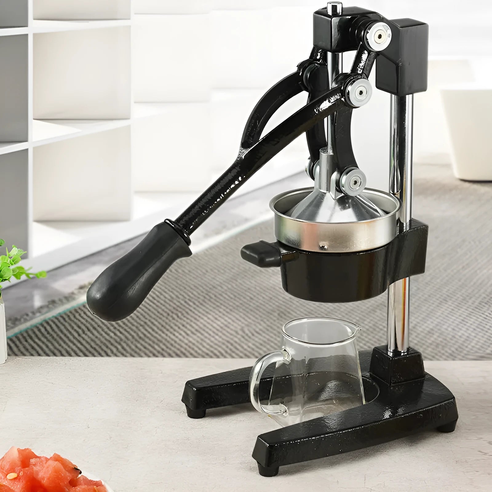 Black cast iron manual juice extractor with stainless steel strainer on a kitchen counter.
