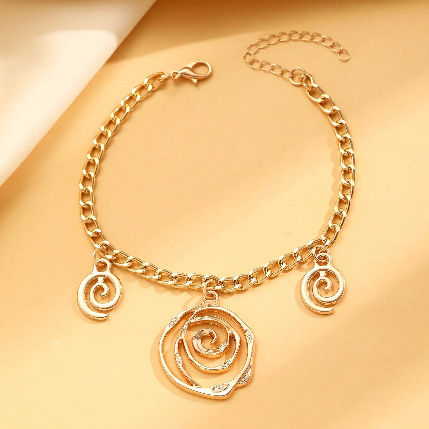 Women's spiral donut charm jewellery set with gold necklace, bracelet and earrings on white background