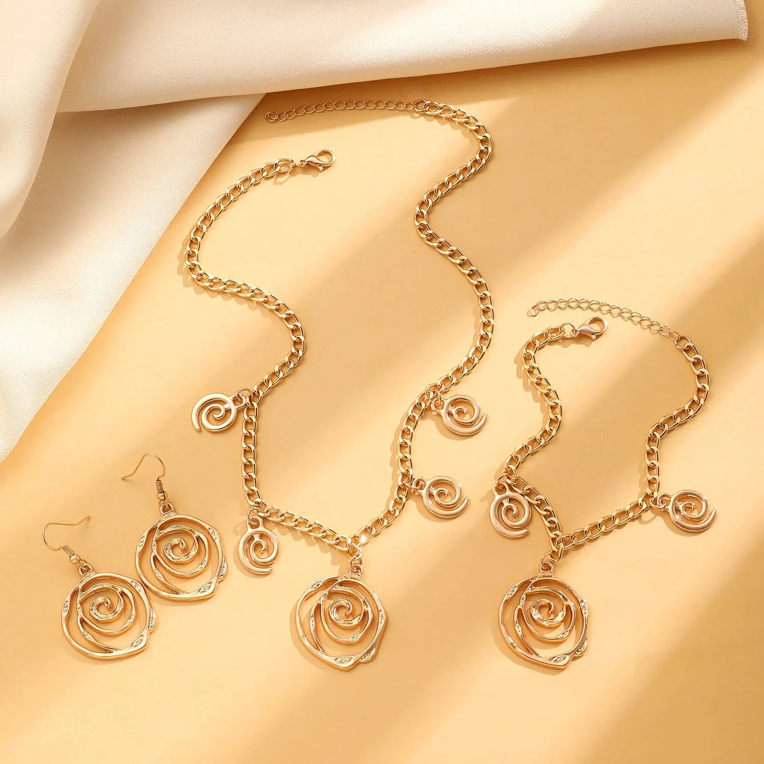 Women's spiral donut charm jewellery set with gold necklace, bracelet and earrings on white background