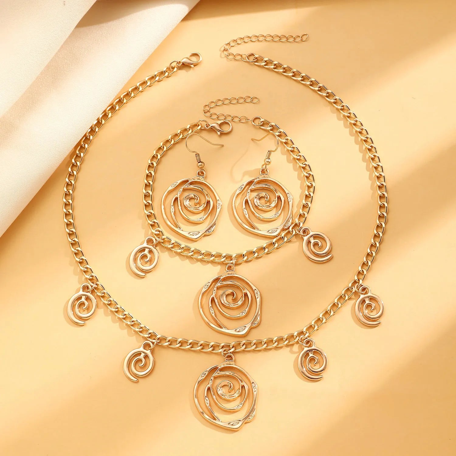 Women's spiral donut charm jewellery set with gold necklace, bracelet and earrings on white background