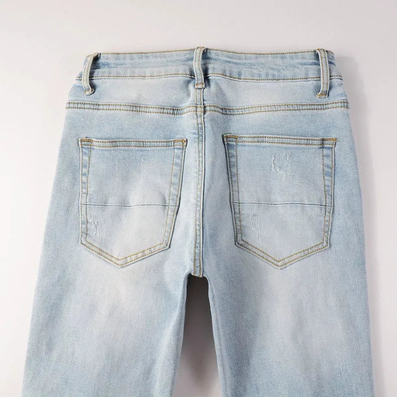 Light blue men's elastic slim fit jeans with hot diamond patch and whisker scrape detailing