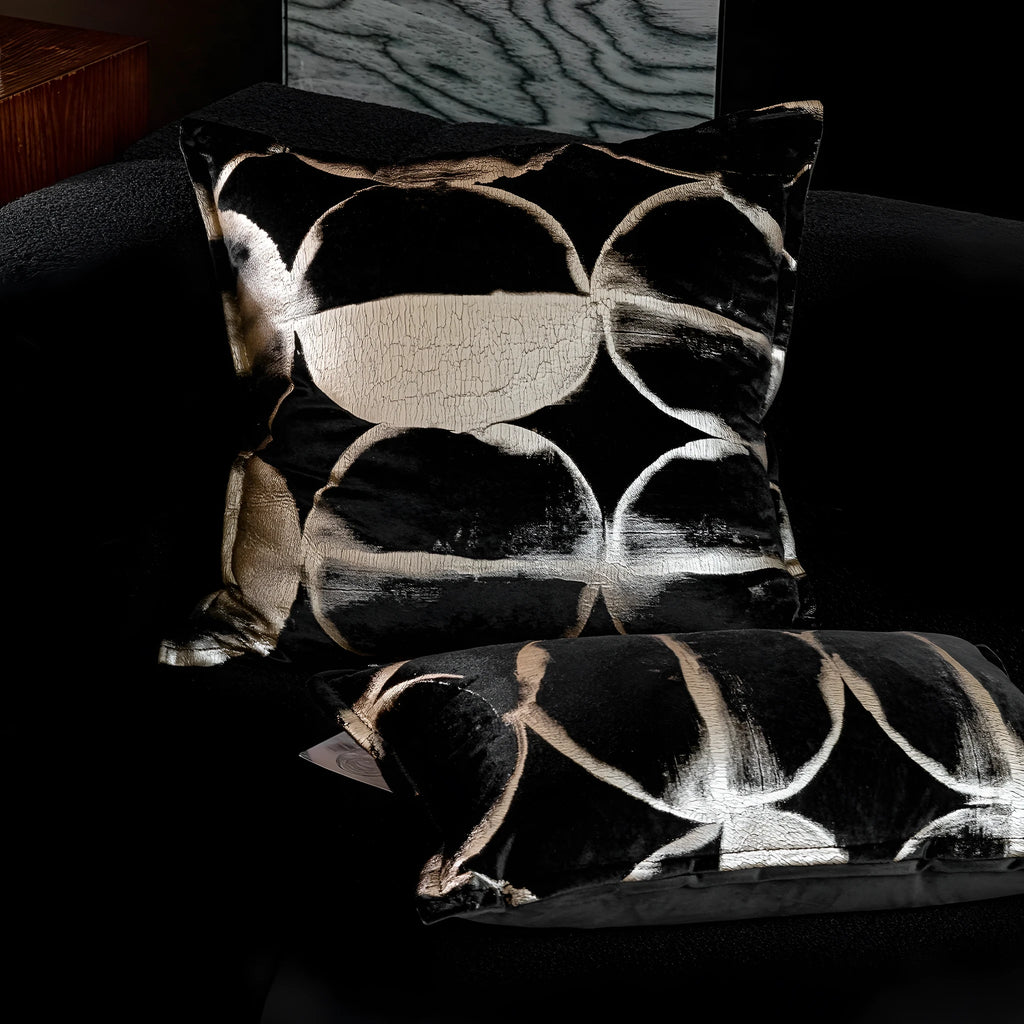 Black and gold abstract pattern decorative cushion cover on a grey sofa.