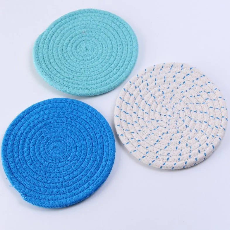 Three round grey cotton cord coasters on a wooden table