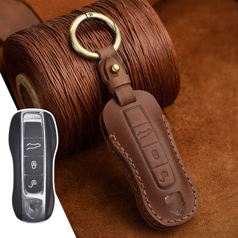 Brown cowhide leather Porsche key cover with a retro metal buckle, shown alongside keys.