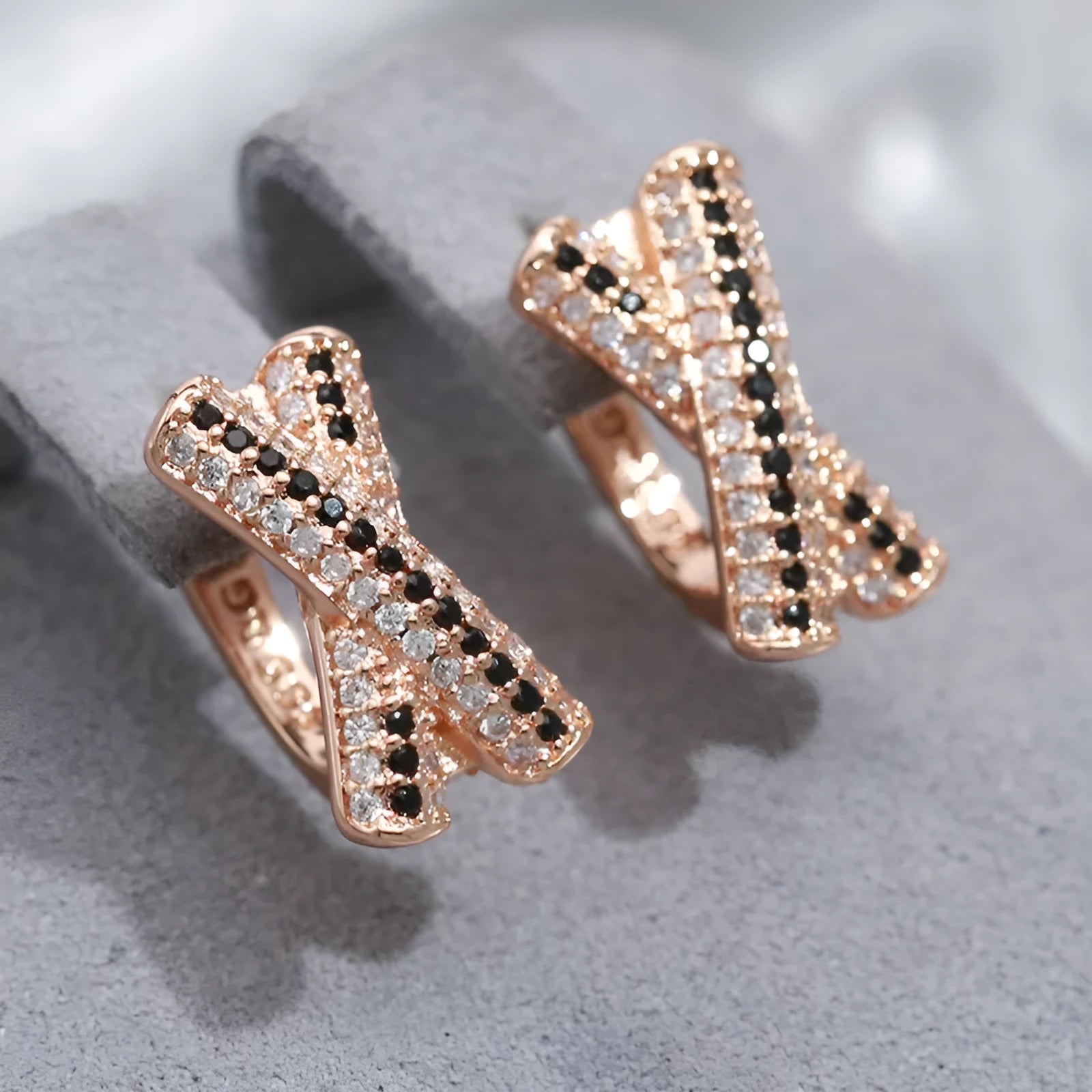 Pair of rose gold copper earrings with hollow-out X-shaped geometric design on light background