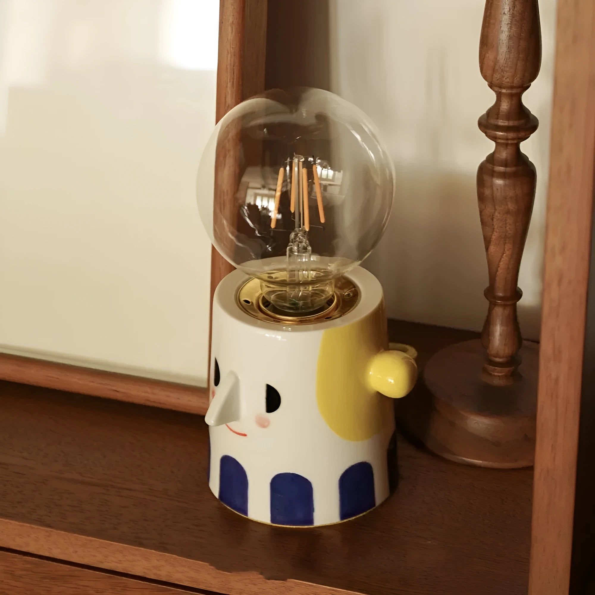 Handmade ceramic bedside lamp with ball headlight colour design on a table.