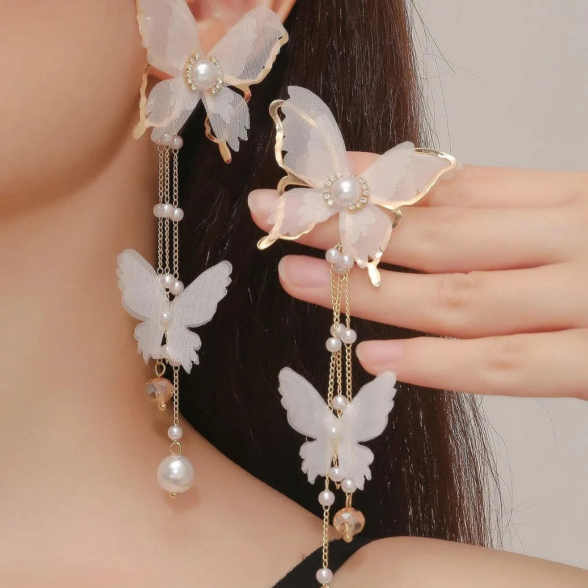 White butterfly-shaped drop earrings with pearls, rhinestones, and tassel lace details on a model.
