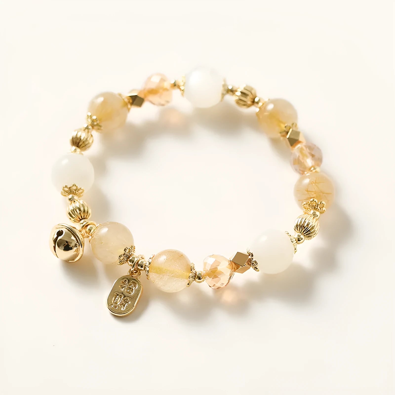 Gold-coloured rutilated quartz bracelet with a ringing bell charm on a wrist.