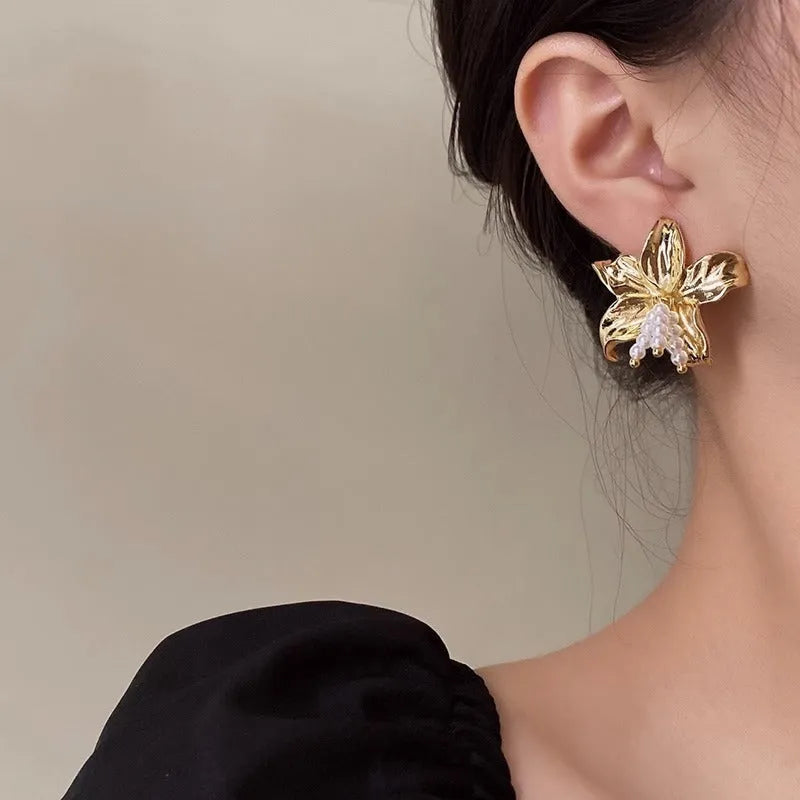 A pair of exaggerated gold metal flower earrings with pearl details, showing a niche jewellery style.