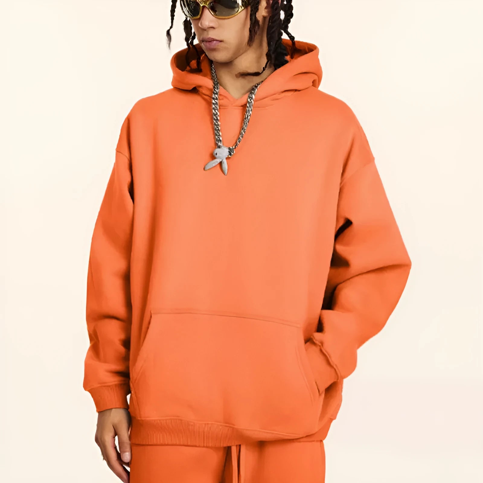 A man wearing a loose-fit, grey, cotton hooded pullover sweater with drop-shoulder sleeves.