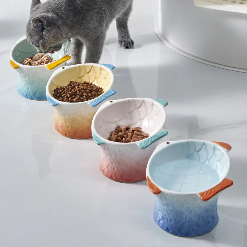 Set of four blue fish-shaped ceramic cat bowls with a tilted angle on a flat surface.