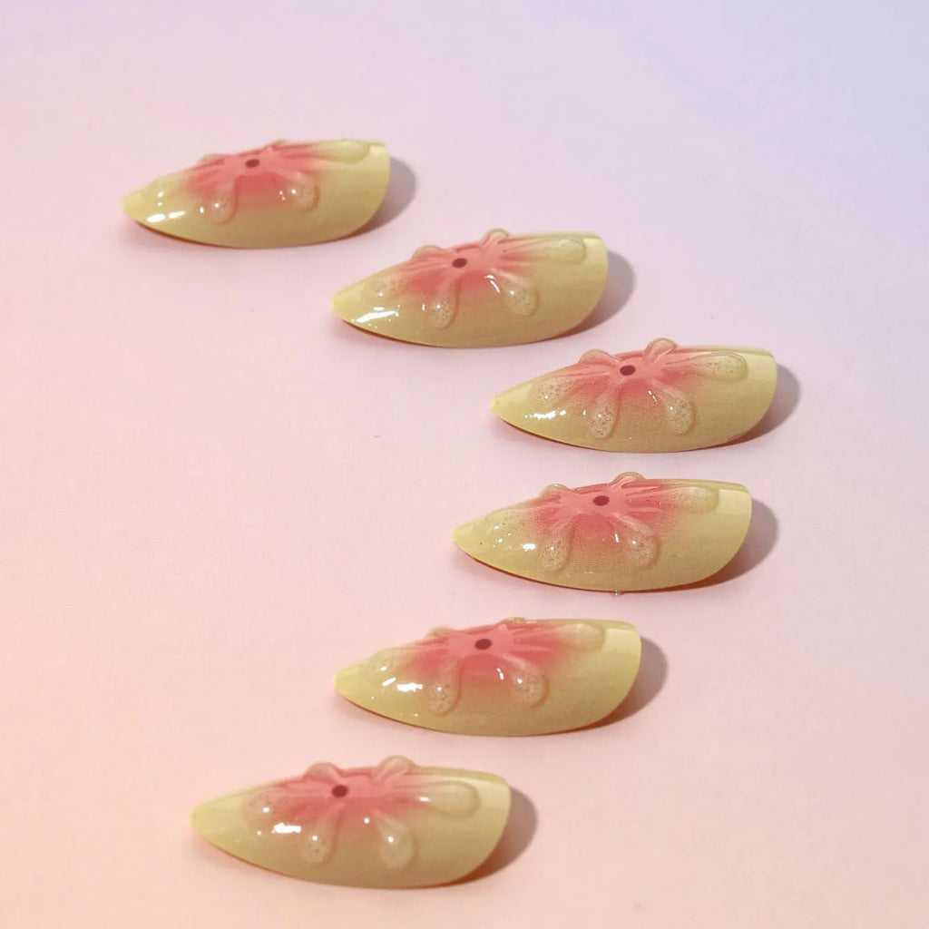 Set of fake nails with colourful 3D cartoon flower designs, jelly glue, and a nail file on a pink background.