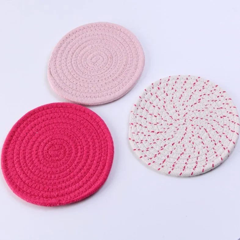 Three round grey cotton cord coasters on a wooden table