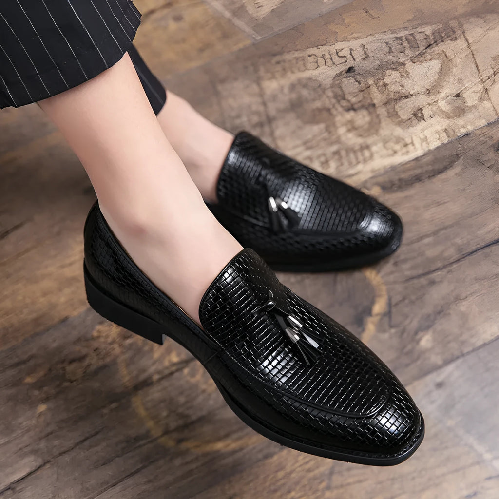 Men's black pointed slip-on leather shoes with a tassel detail on the low-top upper.