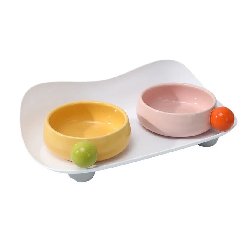 Pink and yellow elevated ceramic pet bowl set for food and water on a non-slip base.