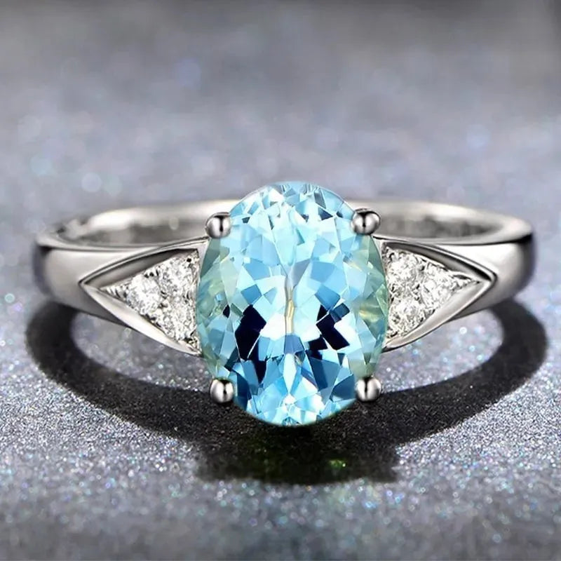 Close-up of a woman's court style ring with a detailed heart pattern inlaid in a blue natural zircon stone.